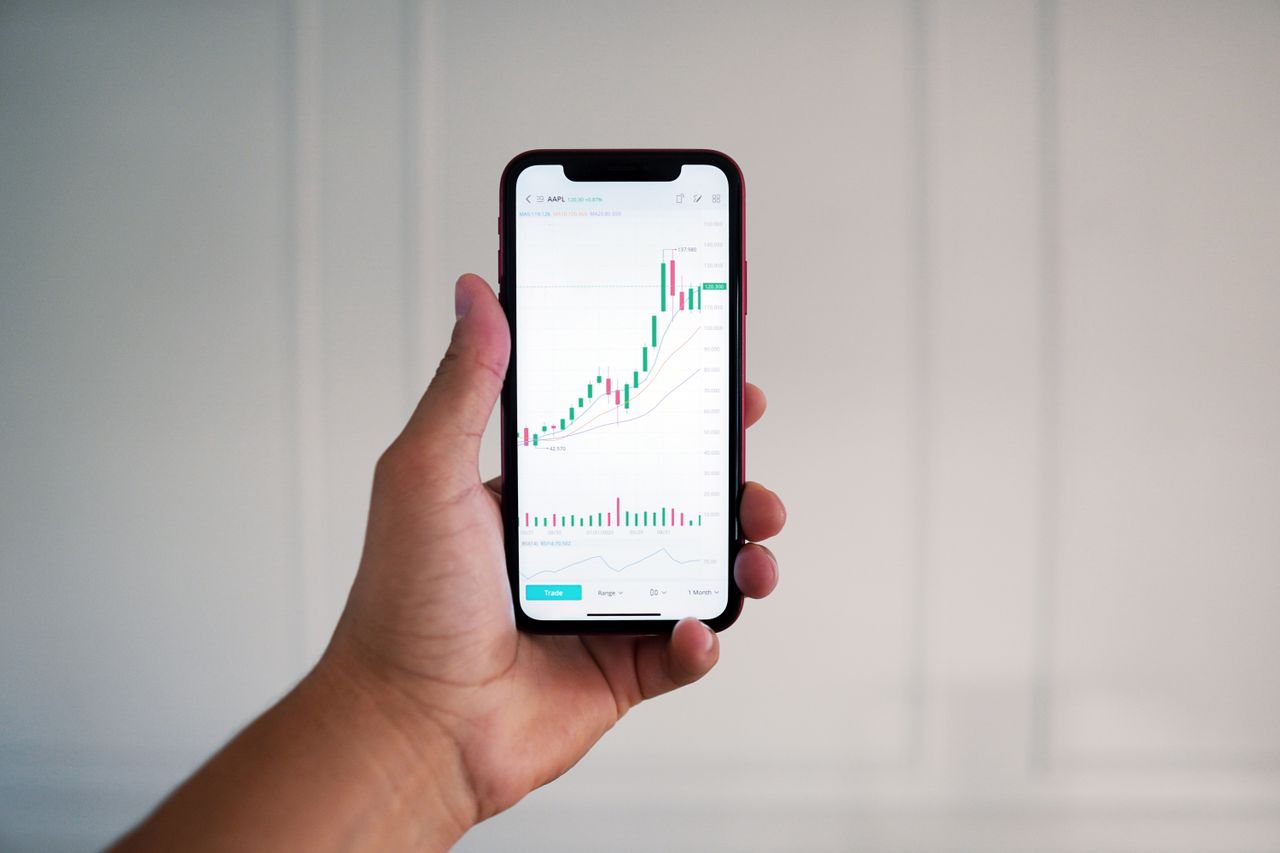 services-03 Close-up of a hand holding a smartphone showing a stock market chart indoors.